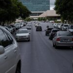 Rua em Brasília com carros estacionados e Câmara Legislativa ao fundo, representando aumento do IPVA e sobrecarga para contribuintes.
