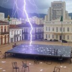 Raio atingindo ato político em Belo Horizonte, causando pânico, com palanque vazio e itens espalhados em praça urbana.
