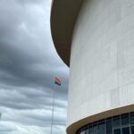 Fachada da Câmara Legislativa do DF em Brasília sob céu nublado, com bandeira arco-íris desbotada, representando falhas no Programa Reconhecer para LGBTQIAPN+.