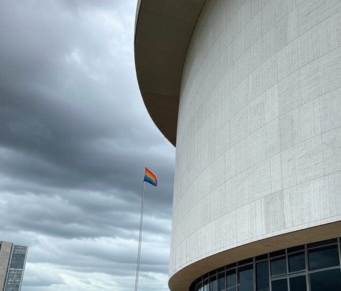 Fachada da Câmara Legislativa do DF em Brasília sob céu nublado, com bandeira arco-íris desbotada, representando falhas no Programa Reconhecer para LGBTQIAPN+.