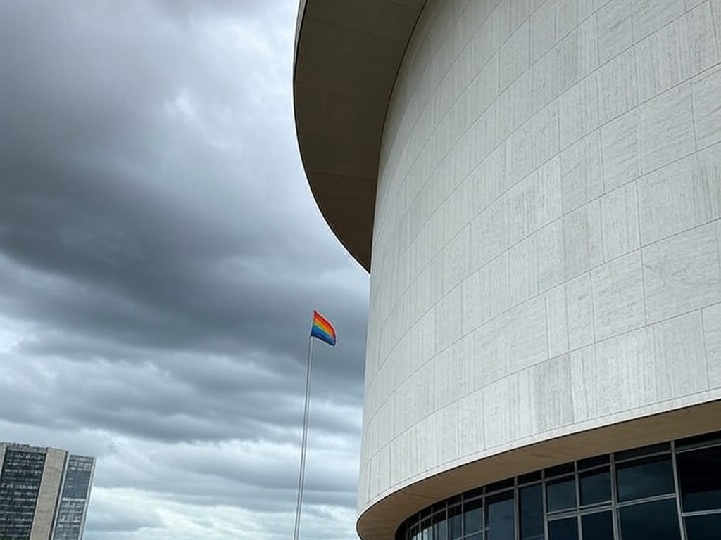 Fachada da Câmara Legislativa do DF em Brasília sob céu nublado, com bandeira arco-íris desbotada, representando falhas no Programa Reconhecer para LGBTQIAPN+.