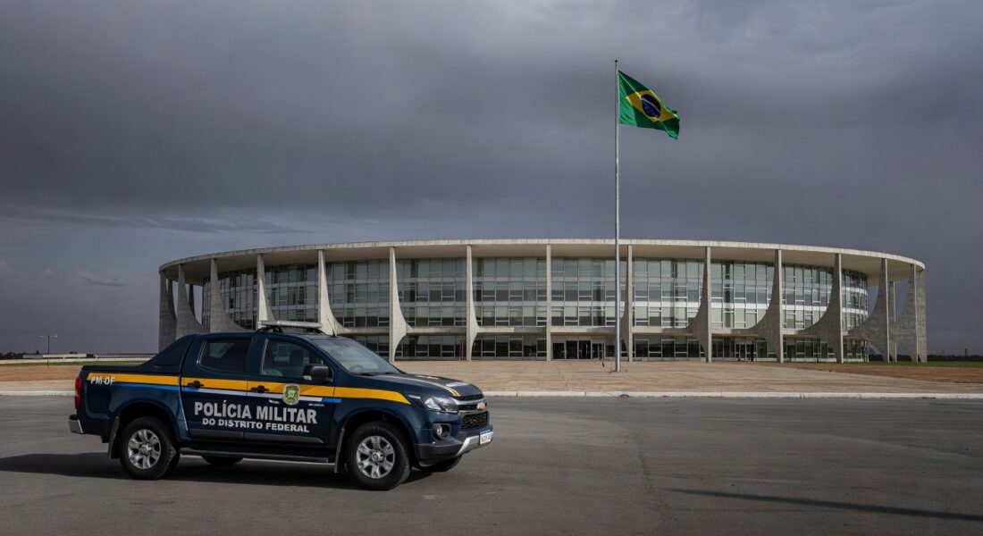 Edifício da CLDF em Brasília com viaturas policiais e fitas roxas simbolizando falhas na reintegração de policiais e combate à violência contra a mulher.