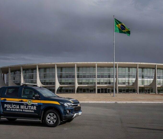 Edifício da CLDF em Brasília com viaturas policiais e fitas roxas simbolizando falhas na reintegração de policiais e combate à violência contra a mulher.