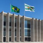 Edifício da Secretaria de Educação do DF em Brasília, com bandeiras do Brasil e DF, em estilo fotojornalístico.
