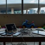 Sala em Brasília com dispositivos eletrônicos rachados e brinquedos, representando vício em telas e danos em crianças.