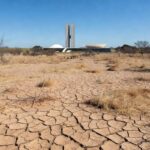 Ponto de hidratação inoperante em Brasília durante seca, com solo rachado e vegetação seca.